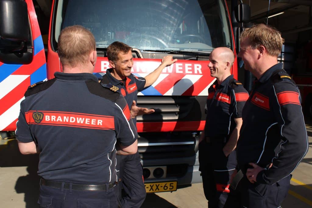 Brandweermensen praten met elkaar, met op de achtergrond een tankautospuit