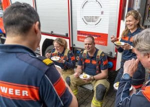 Brandweermensen praten met elkaar bij een brandweerwagen.