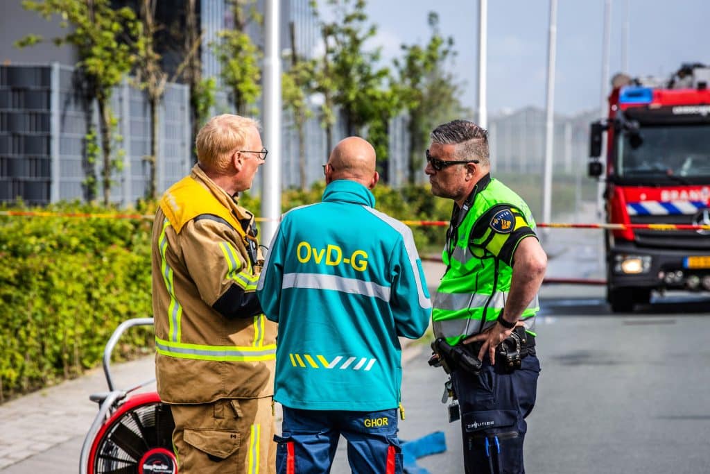 Een brandweerman, officier van dienst geneeskundig (OvD-G) en politieman overleggen met elkaar bij een afzetting bij een incident