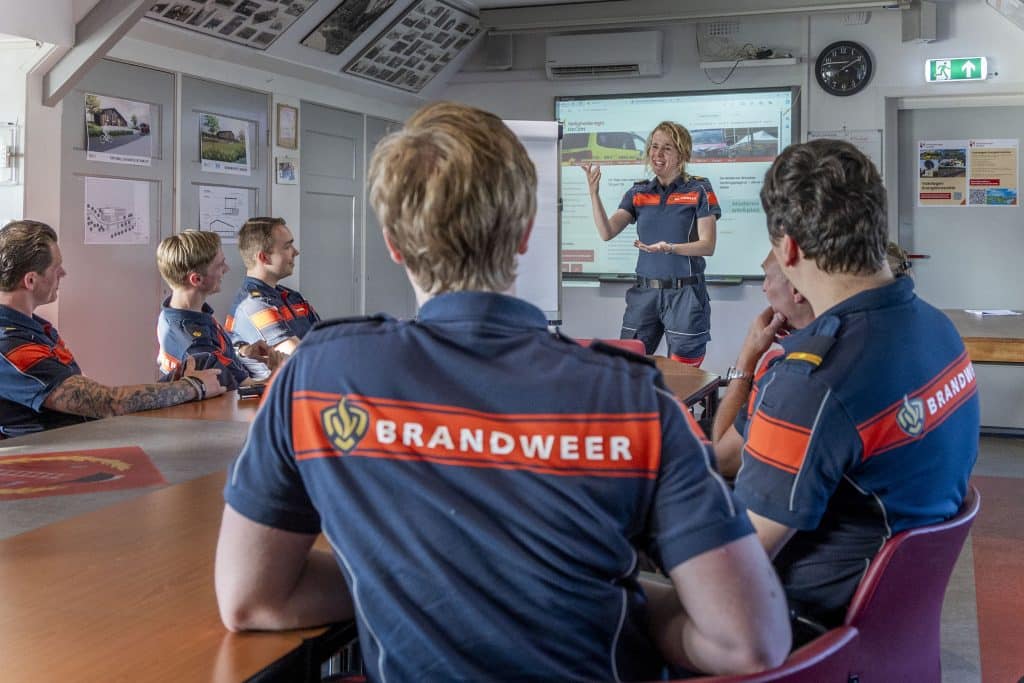 Brandweermensen luisteren naar instructeur op oefenavond in kazerne