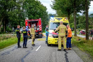 Brandweer, politie en ambulance aanwezig bij een incident waarbij een auto in brand is gevlogen na botsing met een andere auto. De auto raakte van de weg en belandde in een naastgelegen sloot.