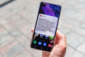 Persoon met smartphone in hand waarop NL-Alert is te zien.