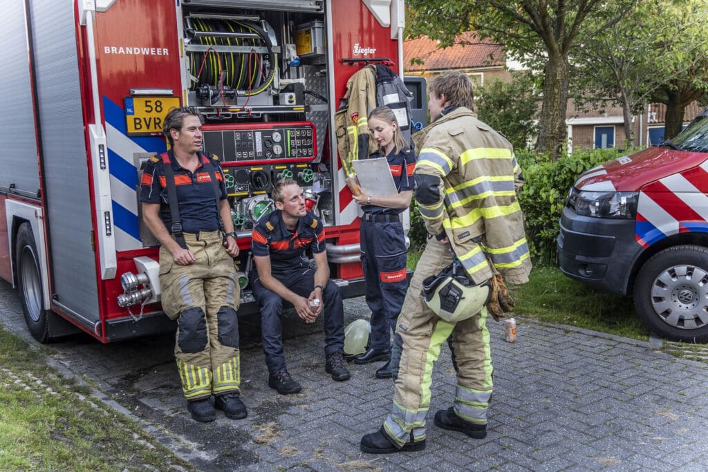 Brandweermensen met elkaar in gesprek bij een tankautospuit.