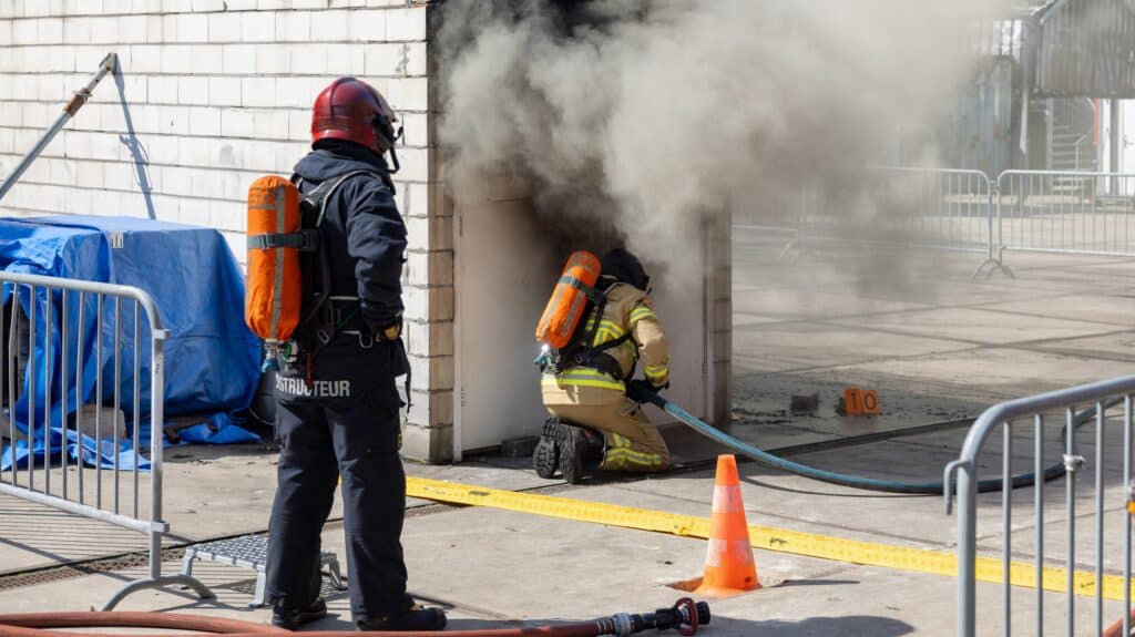 Brandweerman voert slang door bij blussen brand tijdens praktijkexperimenten rookgaskoeling