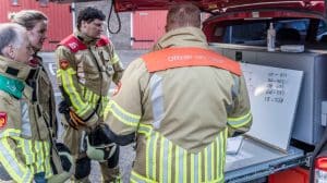 Brandweermensen krijgen uitleg over een oefening bij een brandweerauto